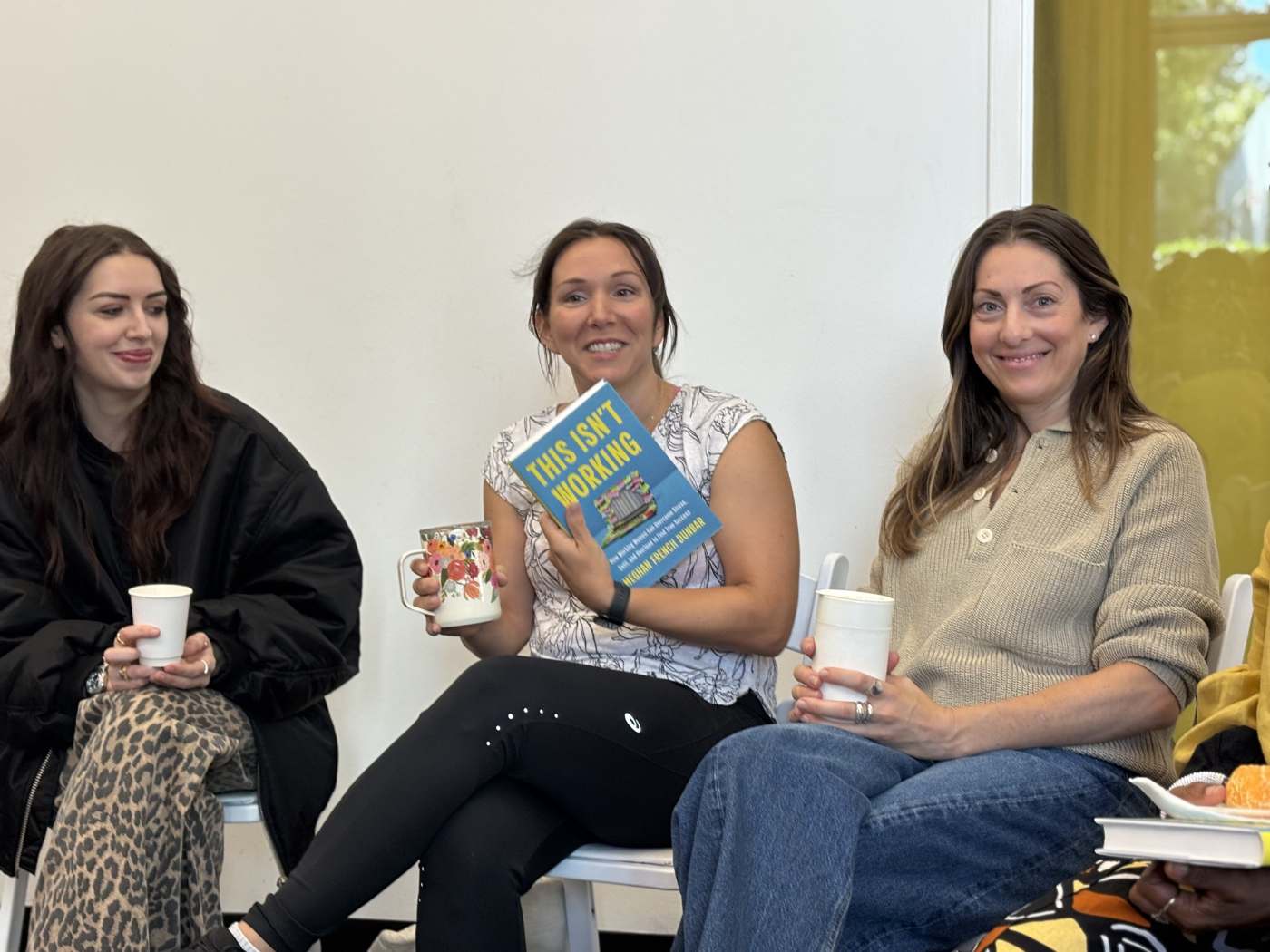 Three women at a reading, one holding up This Isn't Working