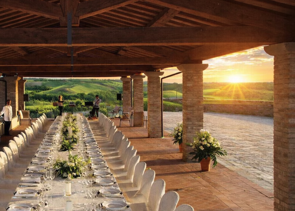 A long table under the villa loggia at sunset, Tuscan hills beyond